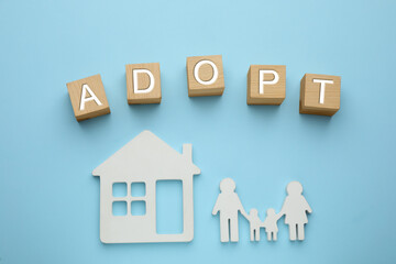 Family figure, house and word Adopt made of cubes on light blue background, flat lay
