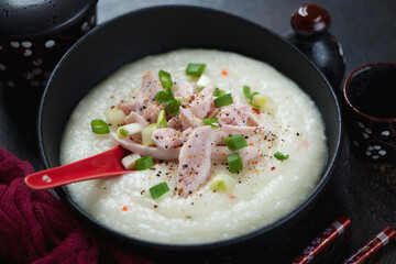 Middle close-up of asian congee with chicken served in a black bowl, horizontal shot, selective focus