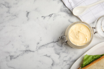 Jar of delicious mayonnaise near fresh sandwiches on white marble table, flat lay. Space for text