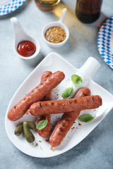 Grilled bratwurst sausages on a shovel-shaped plate with dips and beer, vertical shot on a light-blue stone background