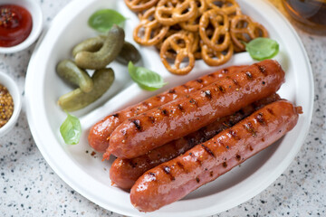 White takeaway plate with traditional german bratwurst sausages, mini pretzels and pickles, closeup, horizontal shot