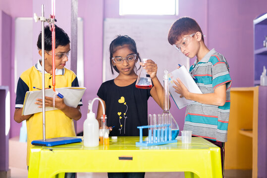 Kids noting down chemicals from falsk by checking at chemistery laboratory - concept of learning reagent reaction, education and knowledge of modern science at school.