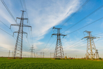 High voltage lines and power pylons and a green agricultural landscape on a sunny day.