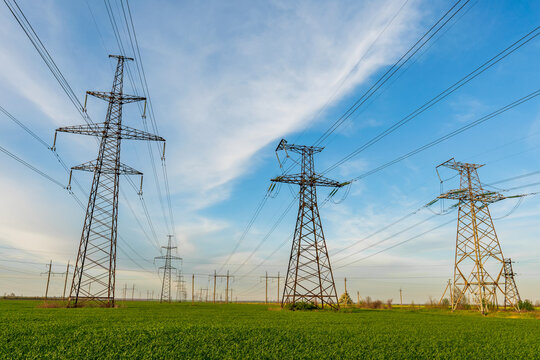 High voltage lines and power pylons and a green agricultural landscape on a sunny day.