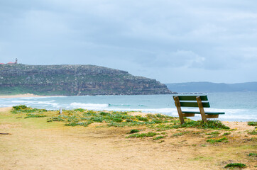 Green Park bench near the ocean, beach shows dark blue sea and horizon clouds sky day at Palm Beach, Northern Sydney, Australia.