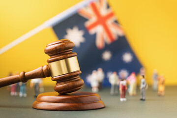 Judge gavel against a blurred Australian flag and plastic toy men background, Australian society...
