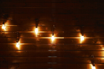 Vintage hanging incandescent lamps on wires. Wooden wall with light bulbs. Loft party interior. Rustic background with copy space.