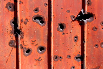 Side of shipping container rusted metal plate heavily damaged by shrapnel during war covered with faded dilapidated paint texture background wallpaper