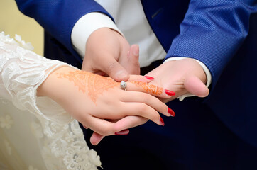 A groom puts a wedding ring on the hand of an Arab bride who puts henna on her hands
