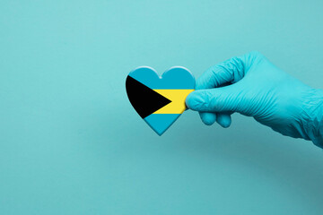 Medical workers hand wearing surgical glove holding Bahamas flag heart