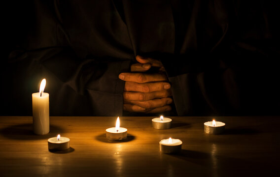 Hands of a monk praying in the dark with candlelights.