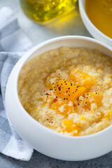 Close-up of millet porridge with pumpkin served in a white bowl, vertical shot, selective focus