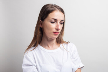 Fototapeta premium Young woman in a white shirt looks into the bottom on a light background