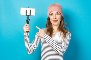 Young woman blogger takes pictures of himself on the phone on a blue background. Concept story, vlog, selfie, blog