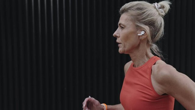 Aged sporty woman jogging outdoors in earphones