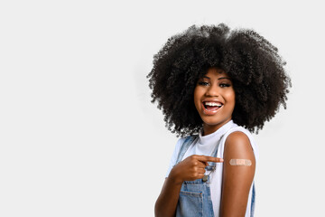 black teenage girl points to sticker on her arm showing she was vaccinated, isolated on gray background.
