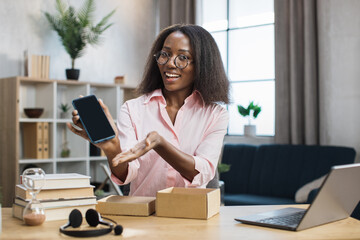 African american woman doing live stream while unpacking box with new smartphone. Female blogger...