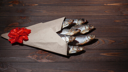 Dry fish in a paper craft bag with a red bow. Brown wood background. February 23. Gift for men. Defenders of the Fatherland Day. St. Patrick's Day. Copyspace. Selective focus.