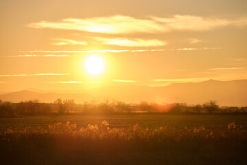 Beautiful evening panoramic landscape with bright setting sun over distant mountain peaks and asphalt road in front at sunset