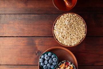 Cereal and various delicious ingredients for breakfast on wooden boards. Dry oatmeal flakes, blueberries, honey and assorted nuts on a wooden background. Copy space. Top view