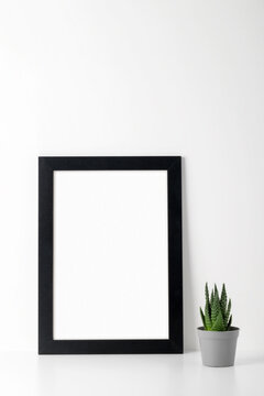 A mock-up of a picture frame with a black wooden frame on a white table, a small succulent. Show text or product.