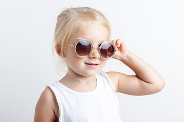 Beautiful blonde child in sunglasses on a light studio background
