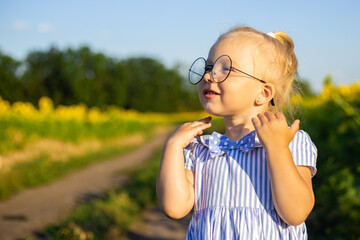 Little girl in a dress and glasses on the background of a sunflower field. Emotional face
