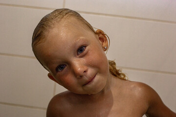 Smiling cheerful child girl with wet hair takes a shower.