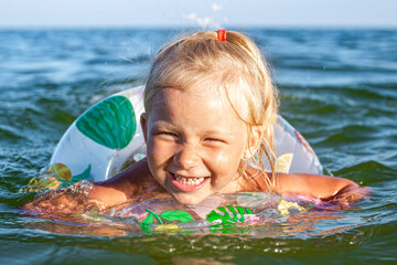 Cheerful child girl swims in the sea with an inflatable ring.