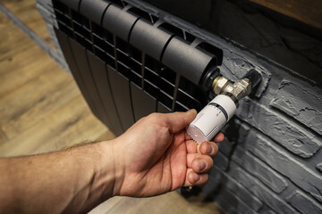 The valve of a home black radiator adjusting the temperature in the room. Hand adjustmen