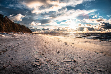 Sunlight shines on the sea waves. The wind blows the waves ashore. In winter, the embankment is icy with stones