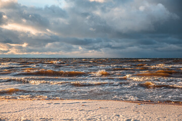 Sunlight shines on the sea waves. The wind blows the waves ashore. In winter, the embankment is icy with stones