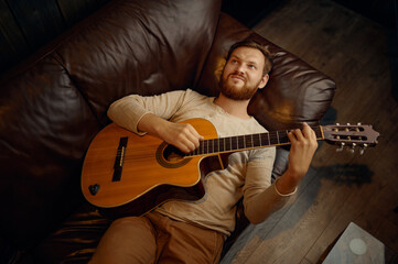 Dreamy man lying on couch playing guitar