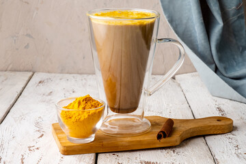 Latte made with turmeric in a large transparent glass on a white table.