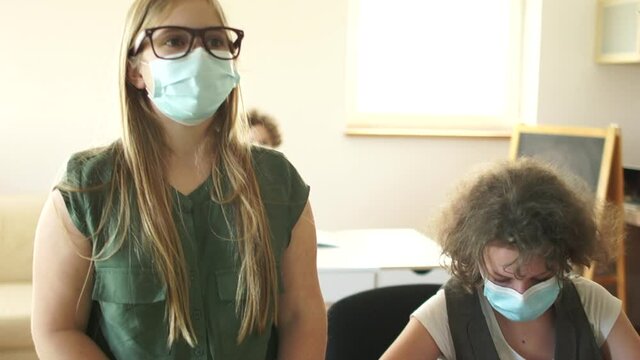 Schoolgirl wearing mask puts her hand up, ready to answer. Children in the class after quarantine coronavirus covid-19, back to school, post-quarantine life, new normality