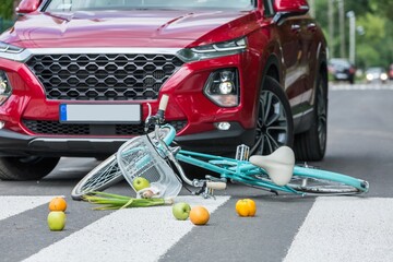 Groceries and a blue bike lies on the street next to the red car that caused the accident