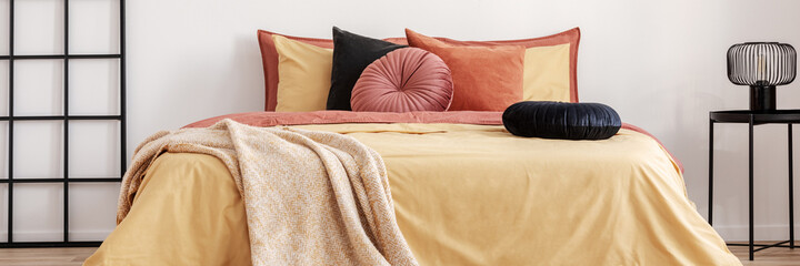 Black round velvet pillow on yellow duvet in trendy bedroom inte