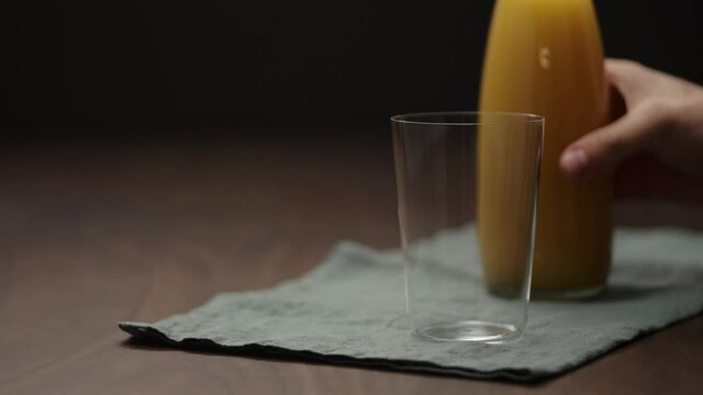 Slow motion pour cold pressed organic orange juice into tumbler glass on wood table