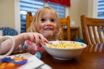 Happy three-year old girl eating breakfast cereal