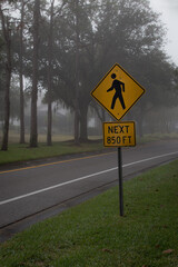 A yellow diamond shape pedestrian crossing sign in foggy weather.