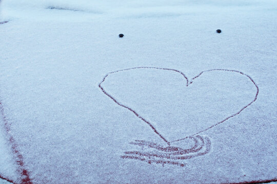the heart is painted on the fallen snow on the hood of a red car. a symbol of love on a winter day
