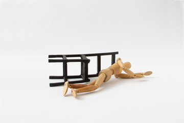 A wooden mannequin fell from a black chair on a white background. The minimal concept of a person who has fallen or is under the influence of alcohol. Drunkenness or fainting.