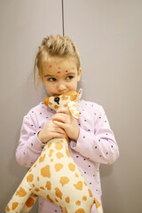 Close up of a cute little girl. Varicella virus or chickenpox rash on a child. Pajamas point and giraffe in hand