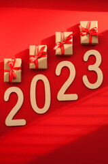 gifts in craft packaging with red ribbons and the number 2023 on a red background with shadows with space for text in vertical format