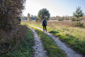 Obraz premium A tourist walks along a country road early in the morning. A man with a backpack on the background of a field illuminated by sunlight.
