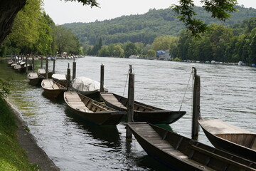 Wooden boats called Weidling in German language moored in a row along riverbank on Rhine river in Schaffhausen, Switzerland. Some of them are covered with tarpaulin.