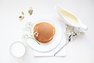 A cup of milk and a plate with a pancakes is on the white table.
