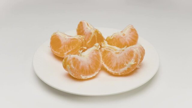 Stop motion. An orange is moving on a white background. Crawls onto the plate and starts spinning. Then the fruit is peeled and starts spinning again. After that, the orange is divided into slices.