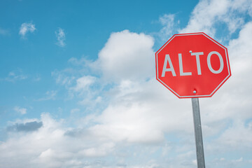 Red Stop sign in Spanish right aligned against the blue cloudy sky background. Alto, wallpaper for text. - 476922561
