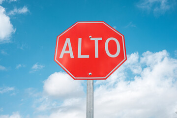 Red Stop sign in Spanish centered against the blue cloudy sky. Alto, background for text space. - 476922567